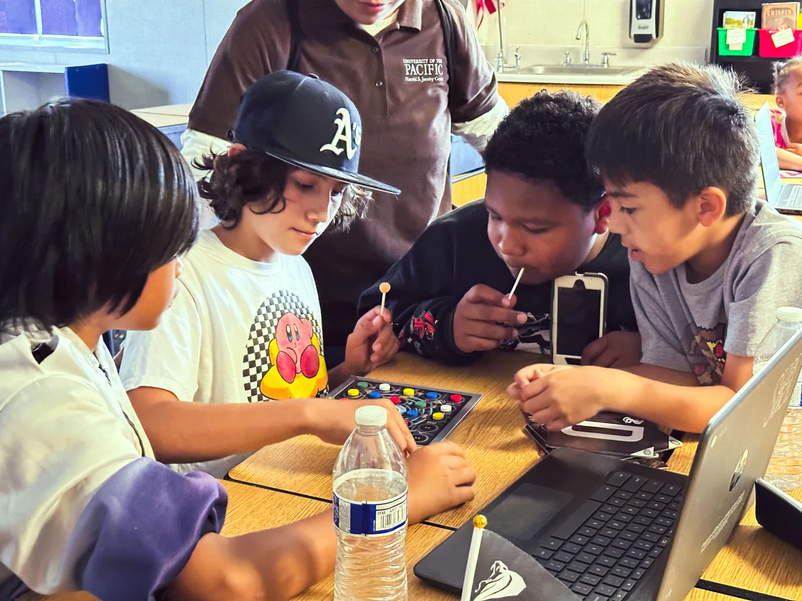 Students crowding excitedly around a hands-on game device